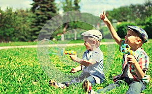 Happy two boys children playing together with toys and blowing soap bubbles in the park on summer day