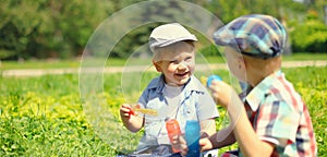 Happy two boys children playing together with toys and blowing soap bubbles in the park on summer day