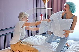 Happy two caucasian women lovely couple sitting on white bed Playing with pillows