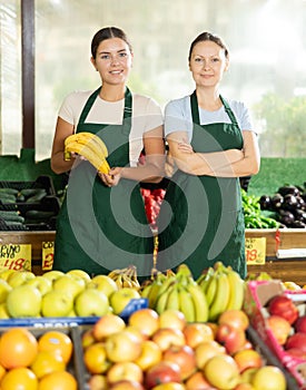 Happy two female sellers wearing apron and standing next to organic foods in supermarket