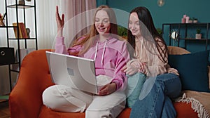 Happy two female women couple family on sofa at home, enjoy chatting, spend leisure time on laptop