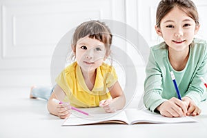 Happy two little girl drawing and do homework on the flloor