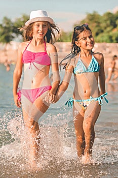 Happy two little girls running together through the water