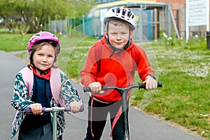 Happy two school kid boy and girl riding scooter in safety helmets. Children biking on the road to school. Child in the