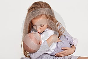 Happy two sisters children posing together isolated over white background, blond female kid kiss her sibling, wearing casual