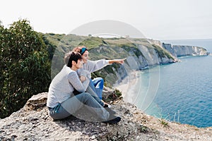 Happy two women friends sitting and looking at beautiful sea landscape on top of the mountain. Friendship and nature concept