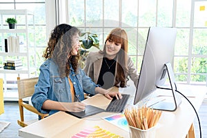 Happy two young female graphic designers discussing with colleague in office. Creative people working together using computer at