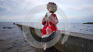 Happy Ukrainian adult woman sitting on river pier smelling bouquet of white roses smiling looking away. Wide shot