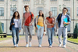 Happy university students walking together on campus, laughing and looking at camera