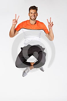 Happy, upbeat masculine athletic young sportsman in activewear, jump, showing peace or victory sign in air, smiling