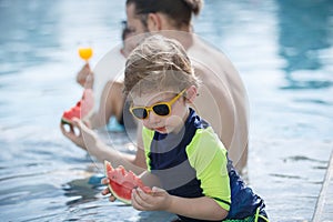 Happy vacation kid boy eat watermelon with family parent have fun enjoy at swimming pool. father and mother with son cheerful