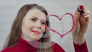 Happy valentine day. Girl draws hearts on glass with lipstick.