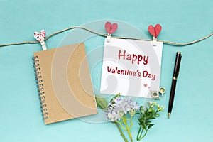 Happy Valentine`s card with blank brown notebook and heart paper clip on blue background