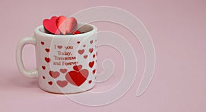 Happy Valentine`s Day greeting card.Holiday Valentine decoration.White glass cup with red glittering hearts on a pink background.