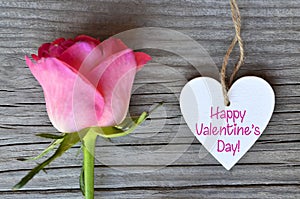 Happy Valentine`s Day greeting card with pink rose and decorative white heart with text on old wooden background.14th of February.