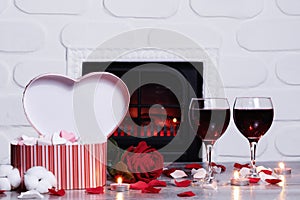 Happy Valentine`s Day, a heart-shaped gift box and two glasses of red wine against the backdrop of a cozy and warm fireplace. Cop