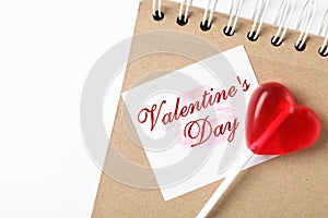 Happy Valentine`s Day. Heart shaped lollipop, notebook and paper note with lipstick kiss on white background, flat lay