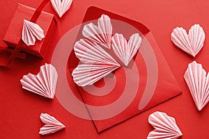 Happy Valentine`s day! Stylish red envelope with pink hearts and gift flat lay on red paper background. Modern valentine card wit