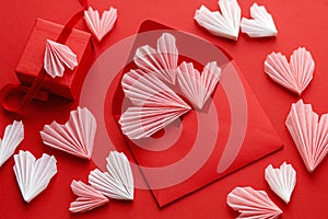 Happy Valentine`s day! Stylish red envelope with pink hearts and gift flat lay on red paper background. Modern valentine card wit