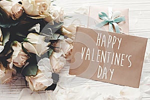 Happy Valentine`s Day text sign on craft greeting card and white roses, gift box on wooden background. Valentines day floral