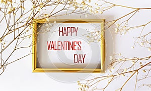 Happy Valentine`s Day written on a gold frame framed with dry white flowers on a white background