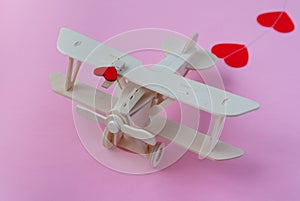 Happy Valentines day. wooden children`s plane on a pink background with red heart, and garland in the shape of a heart