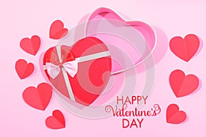 Happy valentines day, opened heart shape gift box with ribbon and small paper hearts with written note, on pink background, top vi