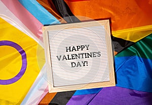 HAPPY VALENTINES DAY text frame on Rainbow LGBTQIA flag made from silk material. Symbol of LGBTQ pride month. Equal