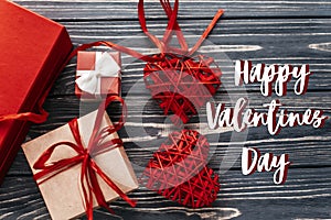 happy valentines day text sign card. stylish red present and heart ribbons flat lay on black rustic wooden background. concept.
