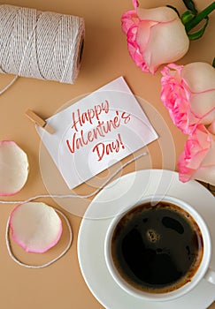 HAPPY VALENTINES DAY text Tender pink rose with white cup of coffee on beige background. Romantic pastel pink rose