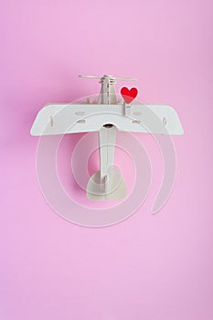 Happy Valentines day. wooden children`s plane on a pink background with red heart