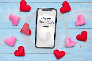 Happy Valentineâ€™s Day word on white touchscreen display of black smart phone with red and pink hearts shape decoration on blue