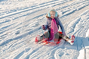 Happy, vibrantly dressed young girl with blue ear muffs sledging down a slope