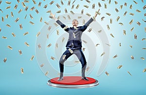 A happy and victorious businessman stands on a giant red button under many falling 100 dollar bills.