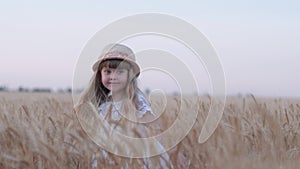 Happy village childhood, little cute girl with straw hat having fun and laughing spins in reaped grain wheat spikes at