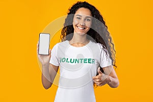 Happy Volunteer Lady Showing Smartphone Screen Gesturing Thumbs-Up, Yellow Background