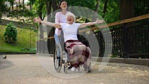 Happy volunteer pushing wheelchair with positive old lady, joyful female patient