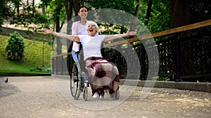 Happy volunteer pushing wheelchair with positive old lady, joyful female patient