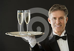 Happy Waiter Carrying Serving Tray With Champagne Flutes