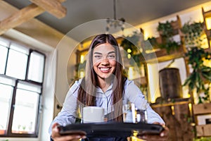 Happy waitress holding tray with cup of coffee, working in cafeteria and serves the table