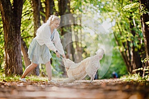 Happy walk with your beloved pet in autumn forest. Young woman in dress is playing with Labrodor Golden Retriever