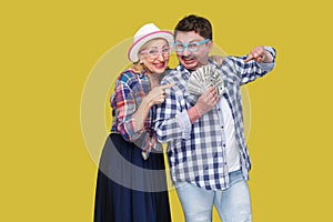 Happy wealthy family, adult man and woman in casual checkered shirt standing pickaback together, holding fan of dollar and