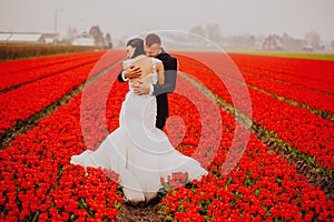 Happy wedding couple breathing fresh air in a colorful field with red flowers