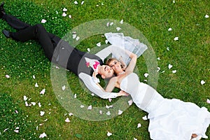 Happy wedding couple lying on green grass