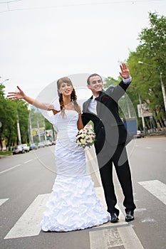 Happy wedding couple standing for a road and wave hands