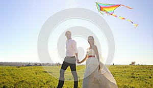 Happy wedding couple walking on green field with flying kite