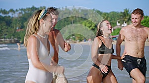 Happy wet group of friends men, women in bikini at tropical trip come out of sea water, flirt, smile, chat. Cheerful