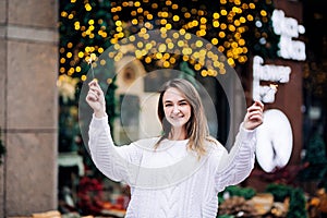 Happy white girl with long dark hair in sweater, garlands in bokeh, holiday cozy atmosphere, smiling woman with bengal