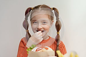 Happy white girl with ponytails eating gyros with a smile. Cheerful kid enjoying Greek fast food meal in restaurant