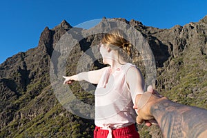 Happy wife holding the hand of his husband and pointing to the mountain, standing and pulling.